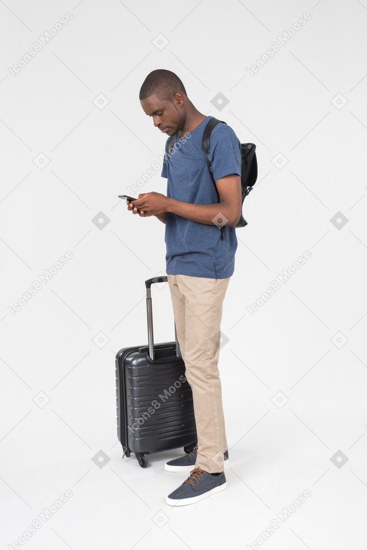 Male black tourist standing near luggage and checking phone