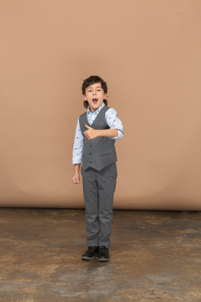 Vista frontal de un chico lindo con traje gris que muestra el pulgar hacia arriba