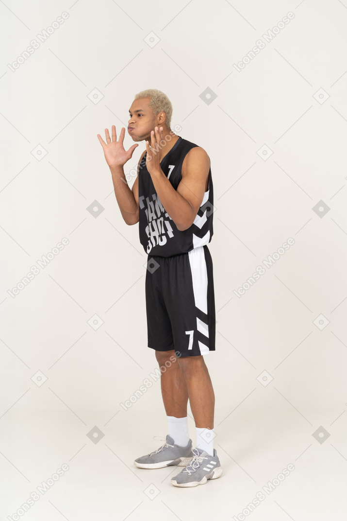 Vista de tres cuartos de un joven jugador de baloncesto masculino soplando mejillas y levantando las manos
