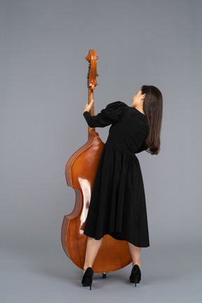 Rückansicht einer jungen musikerin im schwarzen kleid, die ihren kontrabass hält