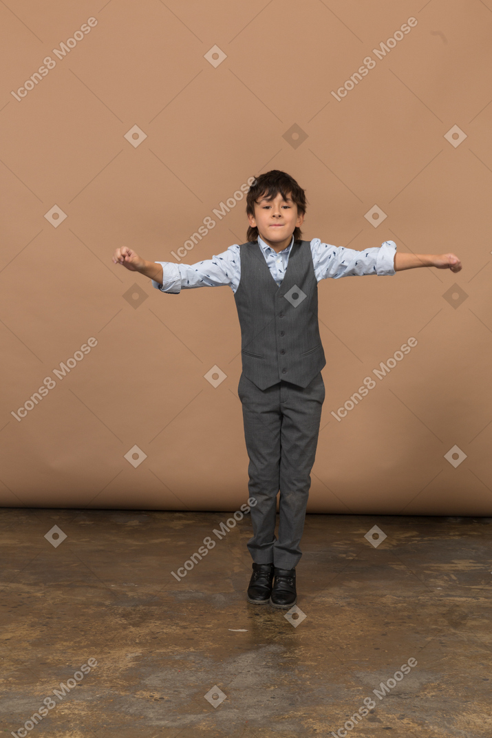 Front view of a cute boy in suit standing with outstretched arms