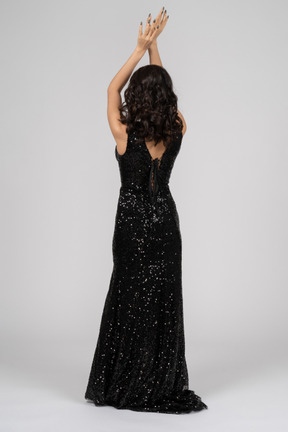 Woman in black evening dress standing back to camera with her arms crossed above