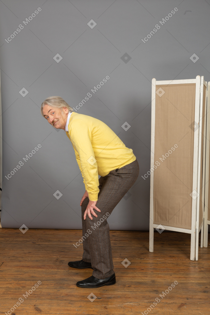 Side view of a curious old man leaning forward while putting hands on legs