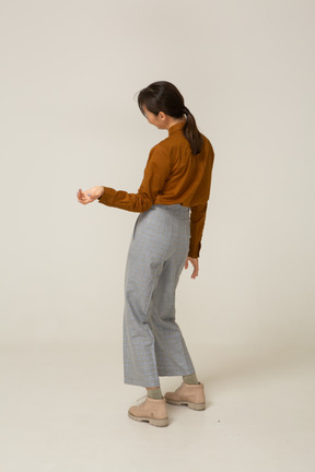 Three-quarter back view of a young asian female in breeches and blouse tilting head and outstretching hand