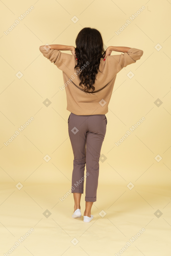 Vista traseira de uma jovem mulher de pele escura tocando seus ombros