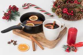 Cup and pan with mulled wine and christmas decorations near it