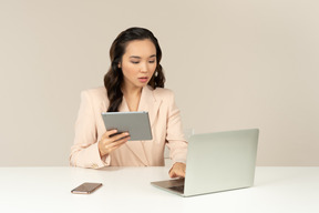 Asiatischer weiblicher büroangestellter, der an laptop arbeitet und tablette hält