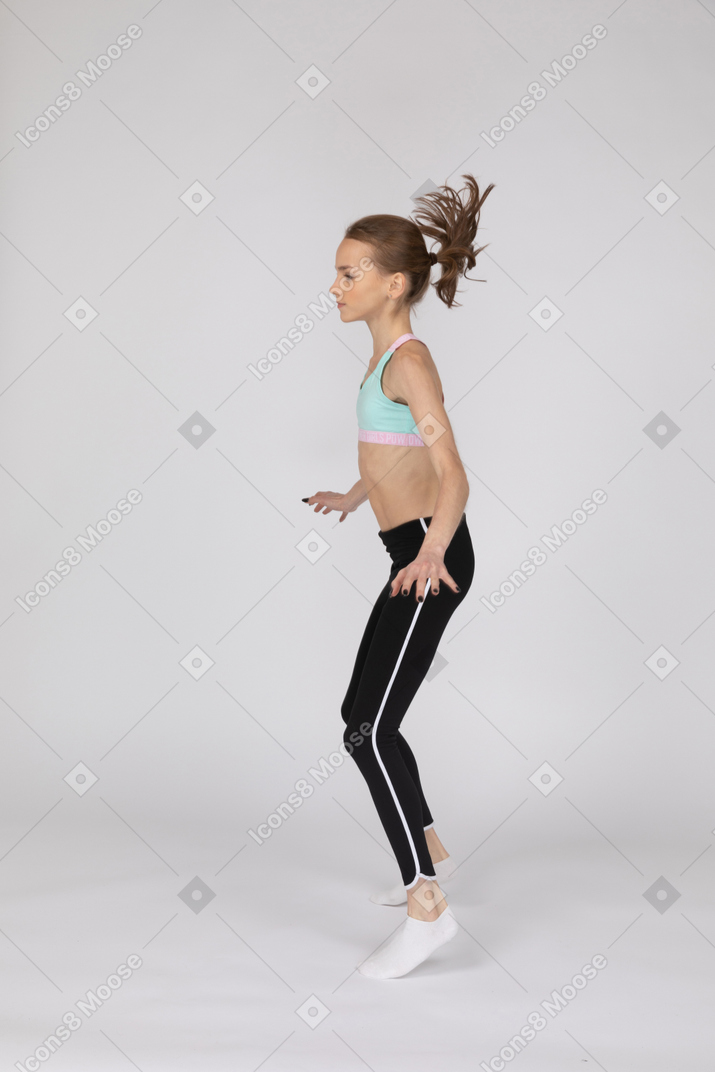 しゃがんで腰に手を置くスポーツウェアの10代の少女の側面図