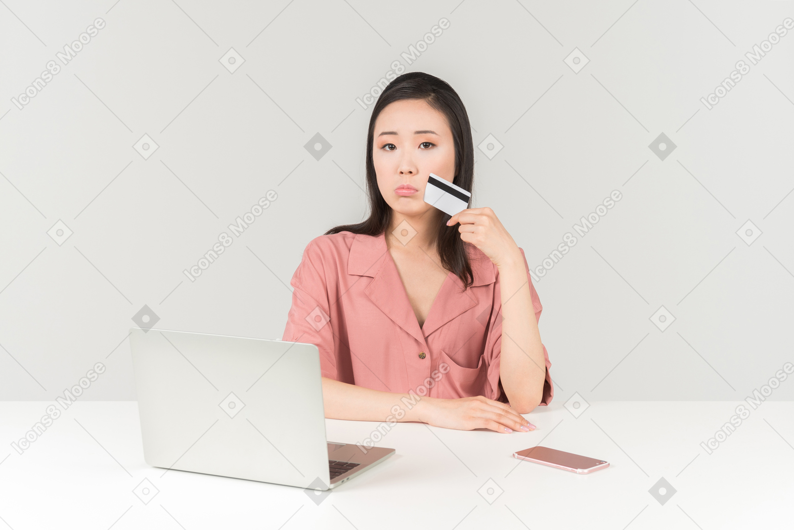 Задумчивая молодая азиатская женщина держа банковскую карточку пока делающ покупки онлайн