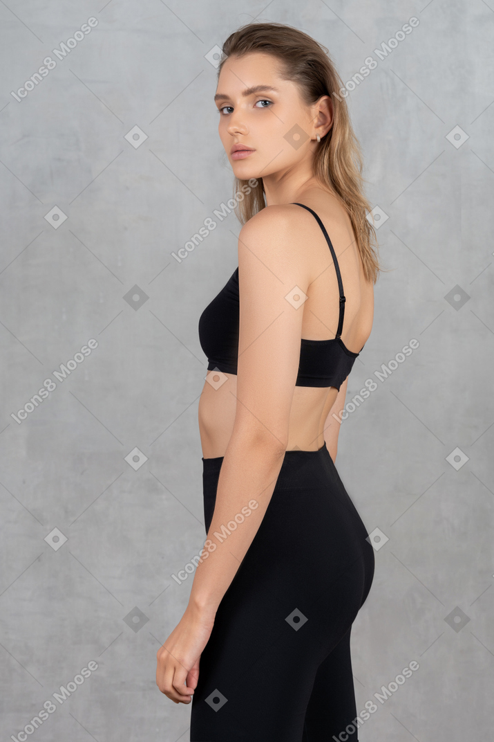 Vista lateral de uma mulher em roupas esportivas pretas, olhando para a câmera