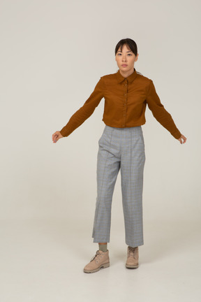 Vista frontale di una giovane donna asiatica in calzoni e camicetta che allarga le braccia