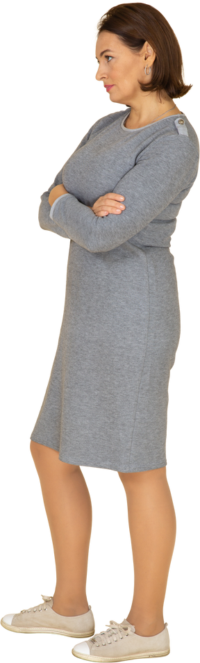 Вид сбоку на женщину в сером платье, стоящую со скрещенными руками