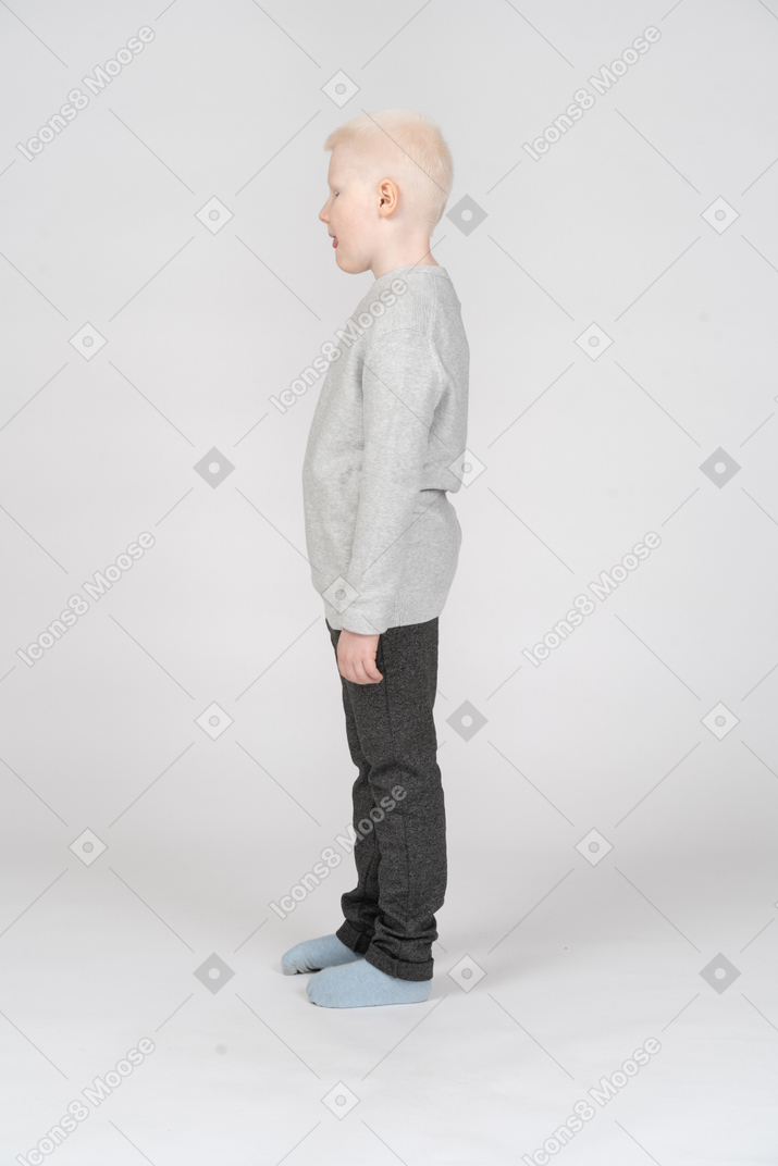 Vista laterale di un ragazzino in abiti casual guardando in basso e aprendo la bocca
