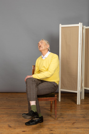 Mann mittleren alters, der auf einem stuhl sitzt und nach oben schaut