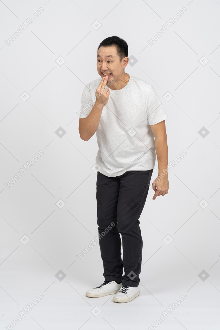 Vista frontal de um homem em roupas casuais, segurando os dedos no lábio e fazendo caretas
