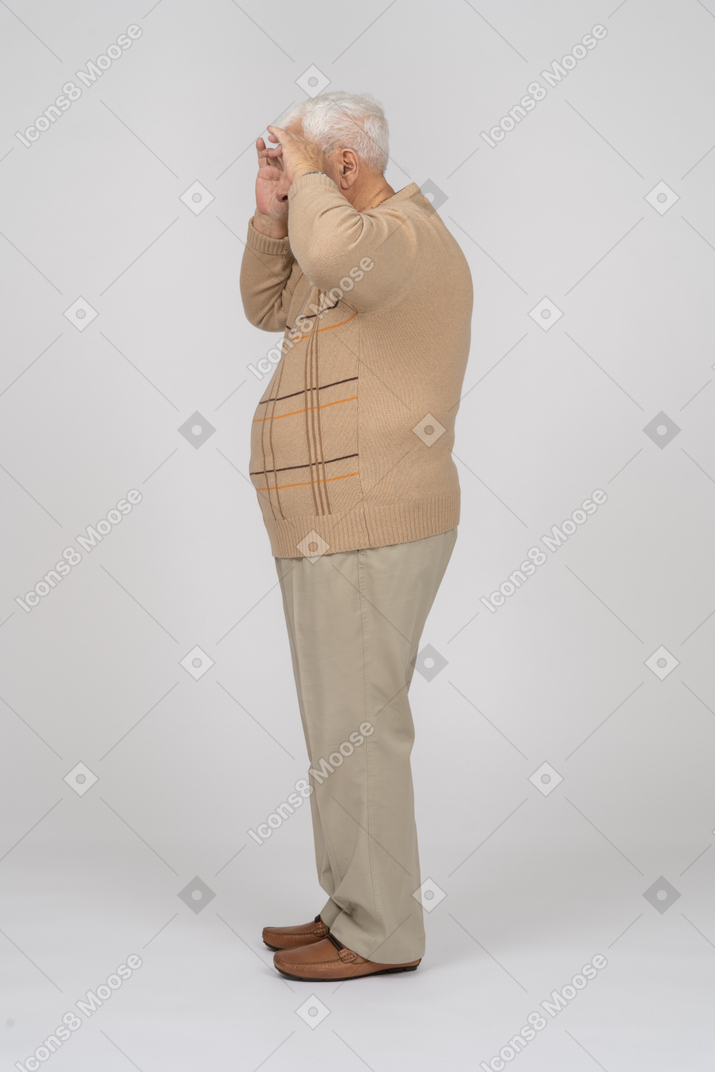 Vista lateral de un anciano con ropa informal mirando a través de los dedos