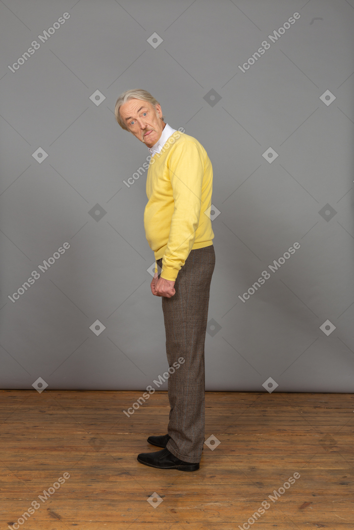 Vista lateral de un anciano sorprendido en jersey amarillo agachándose y mirando a la cámara