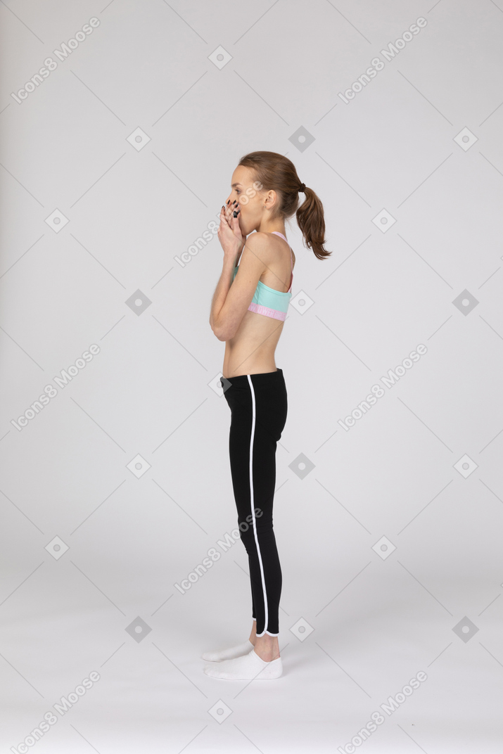 Vista lateral de una conmocionada jovencita en ropa deportiva ocultando su rostro