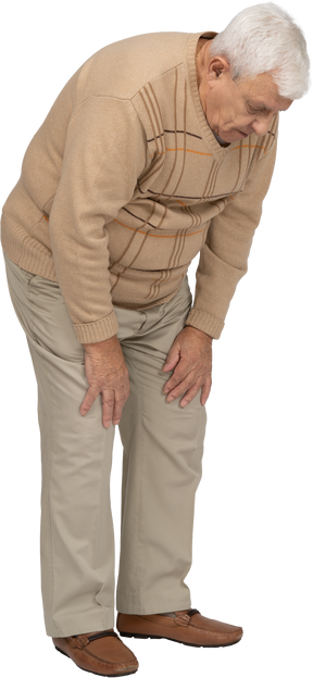 一位身穿休闲服的老人弯下腰，抚摸受伤的膝盖的侧视图