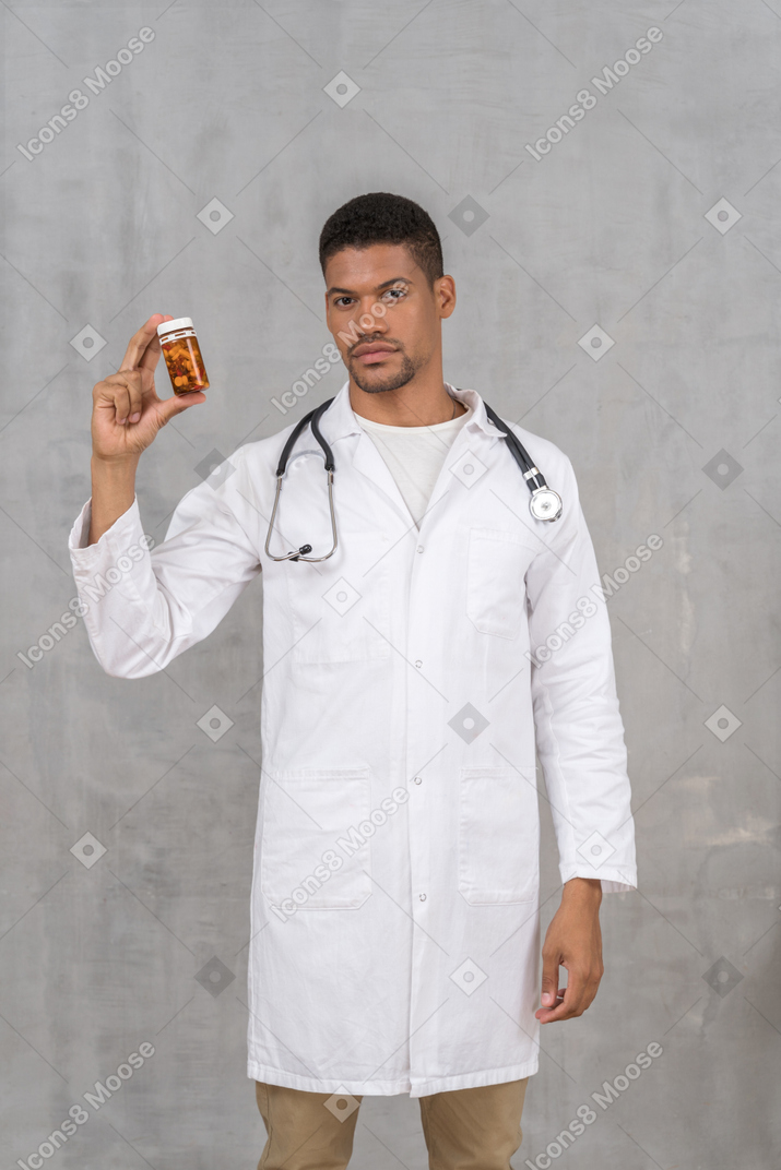 Young doctor in lab coat holding pill bottle
