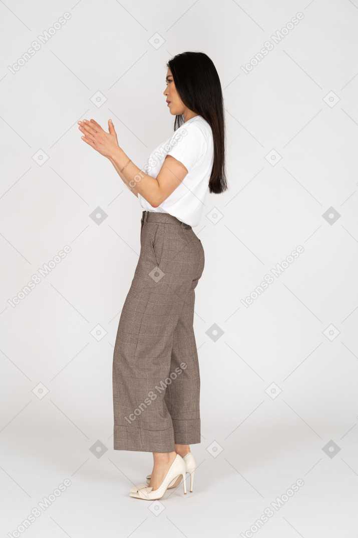 Vista laterale di una giovane donna in calzoni e maglietta bianca che mostra una dimensione di qualcosa