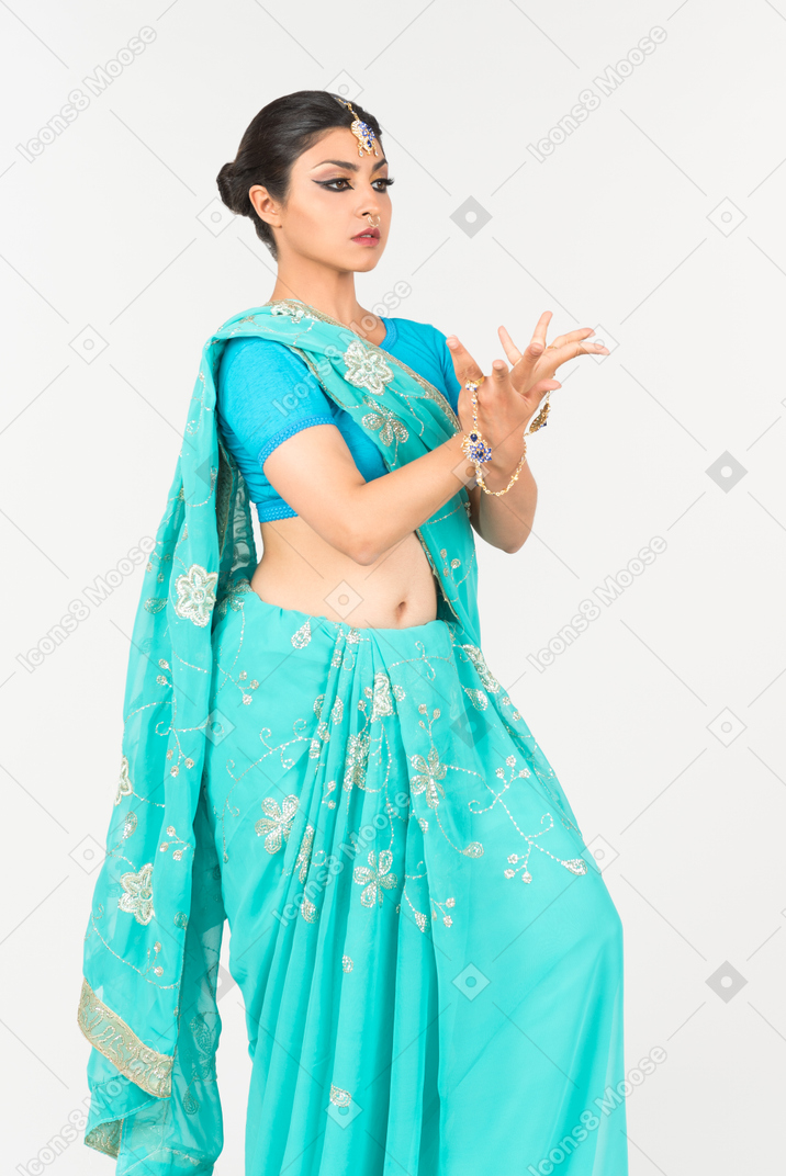 ダンスの位置に立っている青いサリーの若いインド人女性
