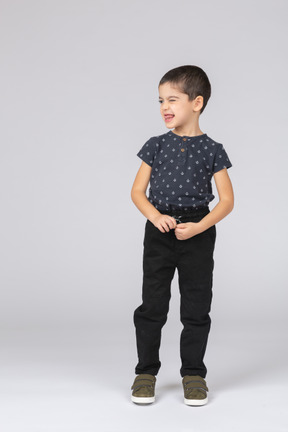 Vista frontal de um menino fofo em roupas casuais olhando para o lado e mostrando a língua
