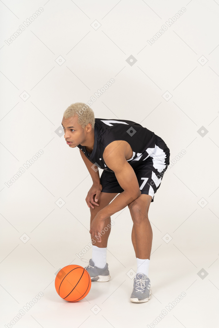 Vista de tres cuartos de un joven jugador de baloncesto de pie junto a la pelota