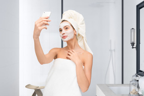 A woman in a towel taking a selfie in the bathroom