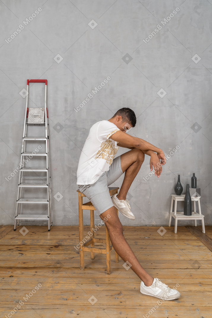 Pensive young man sitting on stool and looking down
