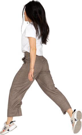 Vista posteriore di tre quarti di una giovane donna che salta in calzoni e maglietta che allarga le gambe