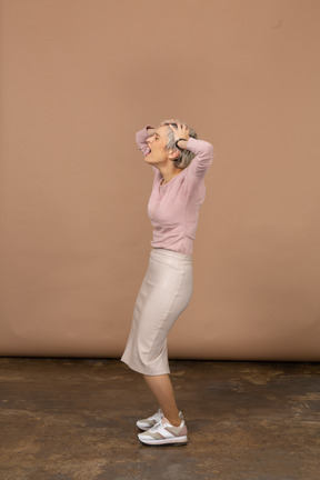 Vista laterale di una donna emotiva in abiti casual in piedi con le mani dietro la testa