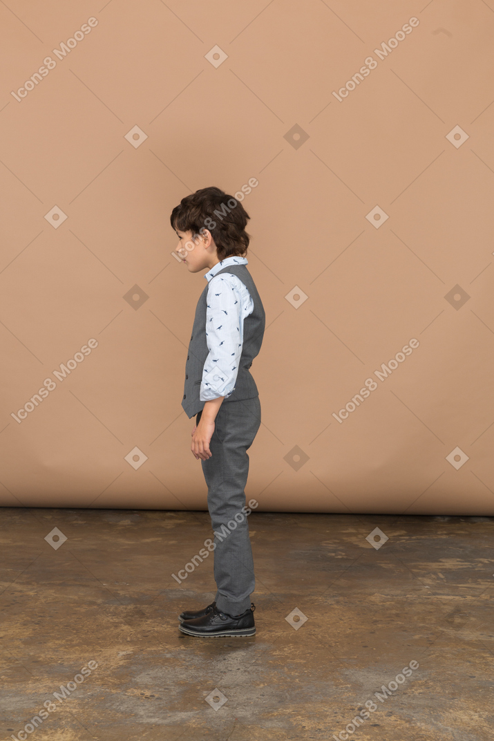 Мальчик в сером костюме стоит в профиль