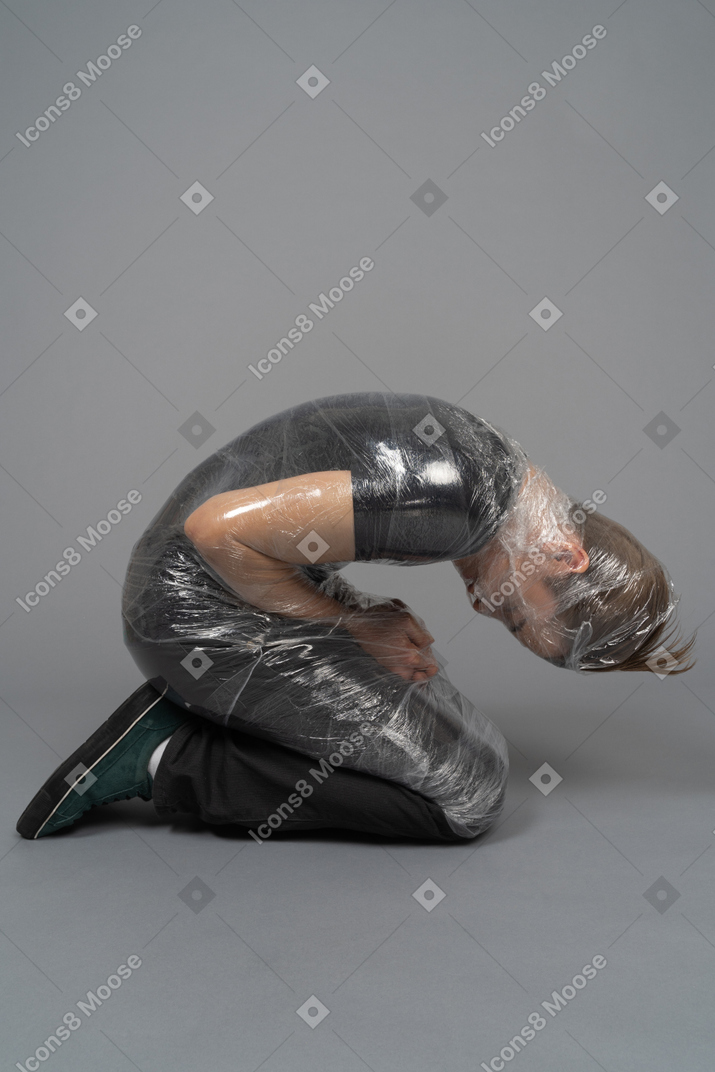 Junger mann auf den knien in plastik verpackt