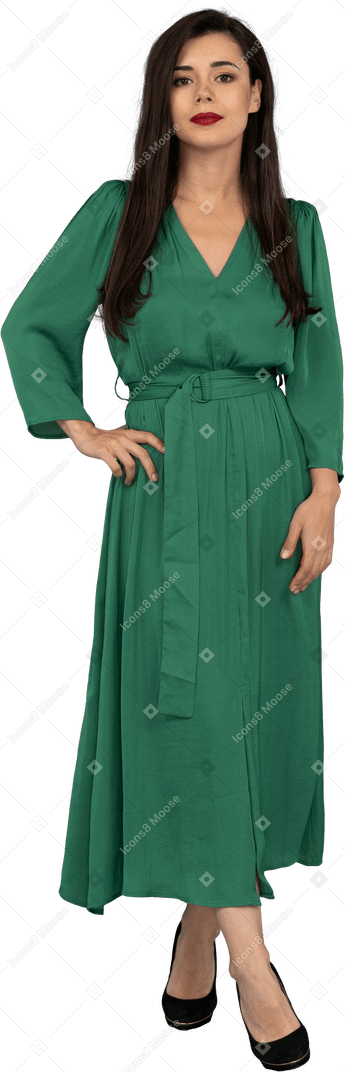 Vista frontal de uma jovem de vestido verde colocando a mão no quadril