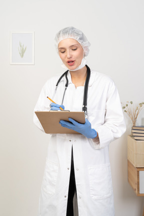 Vista frontal de uma jovem médica fazendo anotações em seu tablet