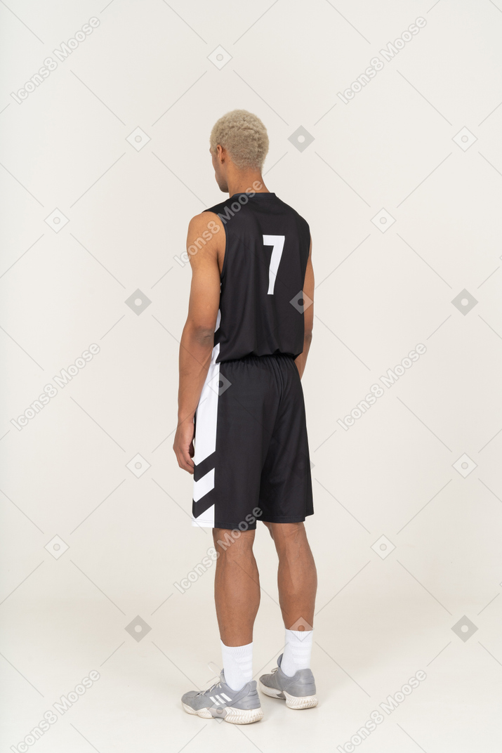 Трехчетвертный вид сзади молодого баскетболиста, стоящего на месте и смотрящего в сторону