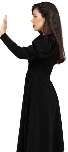 Vista lateral de uma jovem em um vestido preto levantando a mão