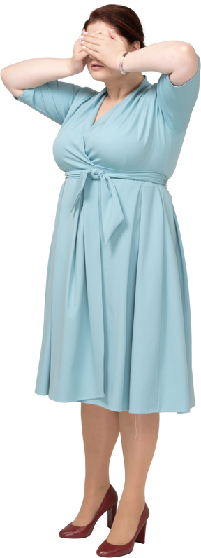 Front view of a woman in blue dress covering eyes with hands