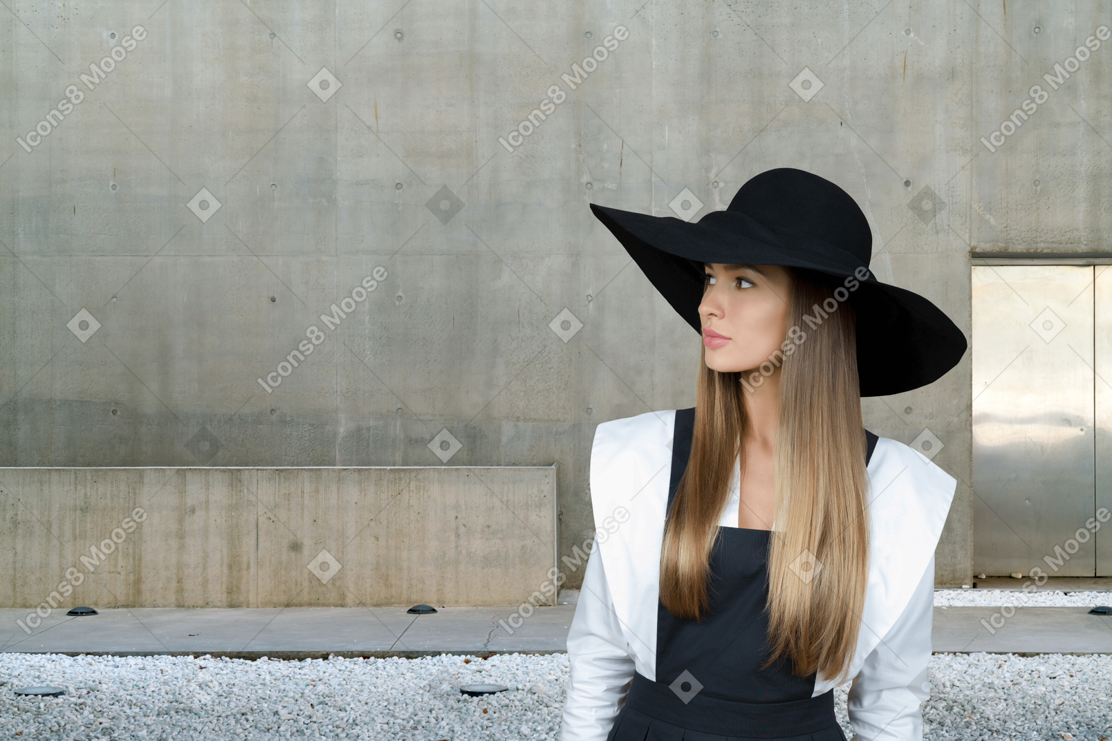 A young woman in a black hat and a white shirt sits in front of a wall