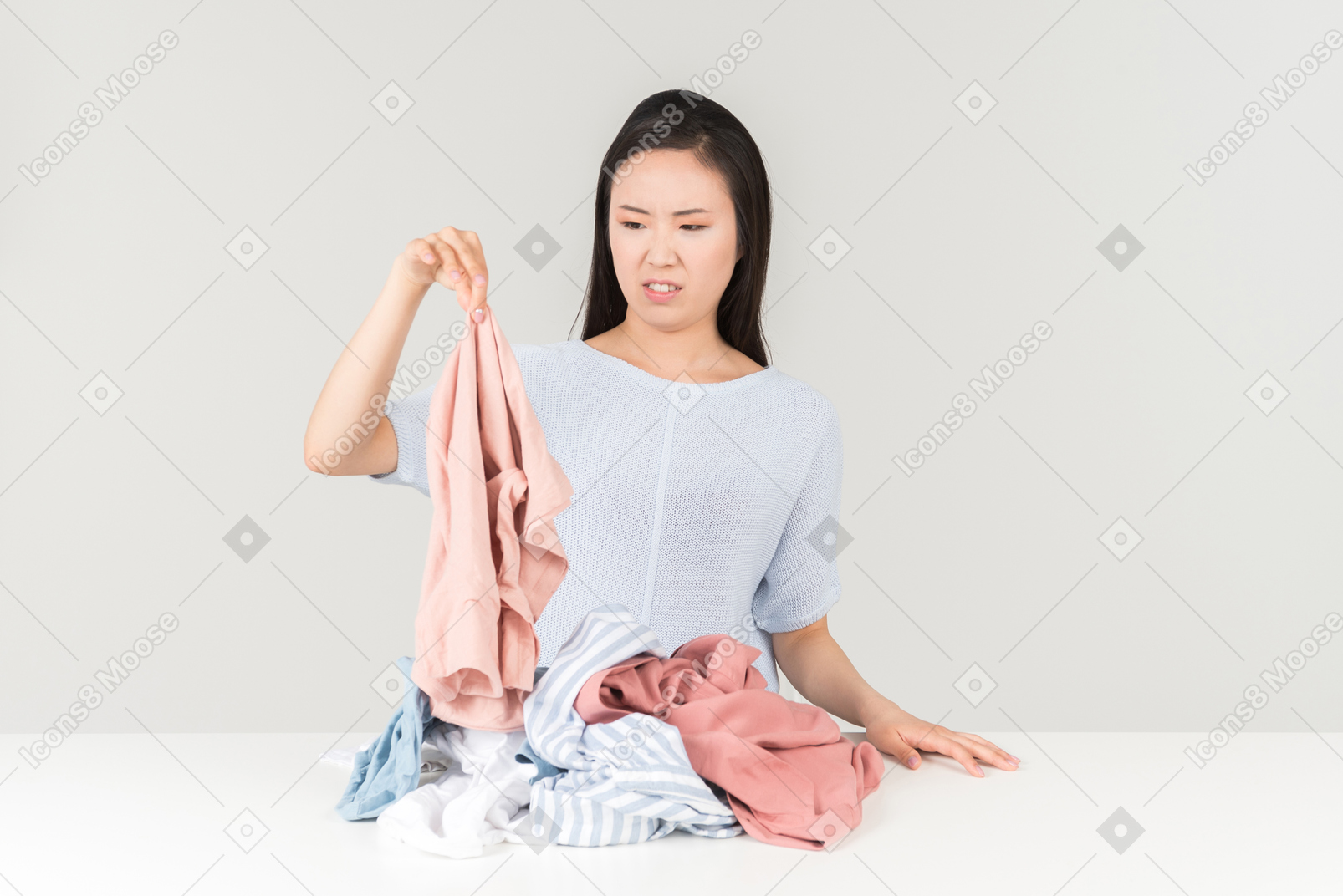 Giovane donna asiatica è disgustata con la pila di vestiti sul tavolo