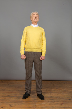Vorderansicht eines alten neugierigen mannes im gelben pullover, der kopf anhebt und kamera betrachtet