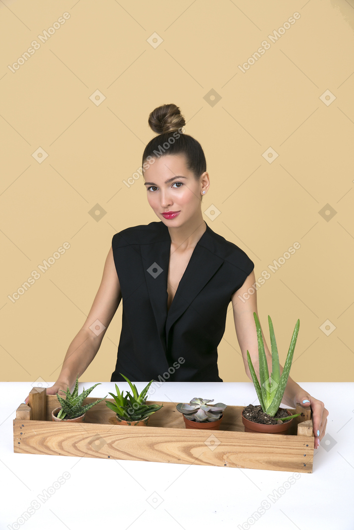 Mujer hermosa joven sentada junto a una caja de madera con algunas plantas caseras en ella