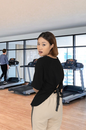 A woman standing in front of a treadmill in a gym