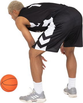 Three-quarter back view of a young male basketball player standing by the ball