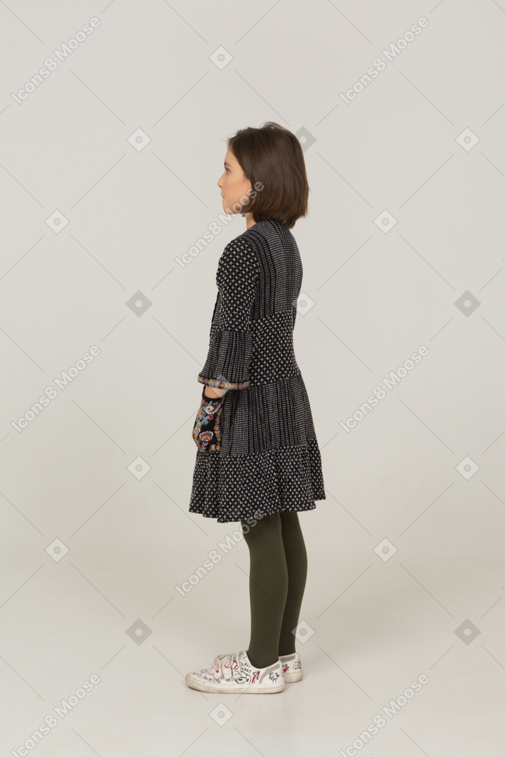 Vista lateral de uma menina de vestido colocando as mãos nos bolsos