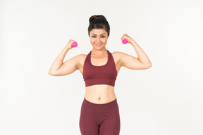 Young indian woman in sportswear lifting hand weights with both hands