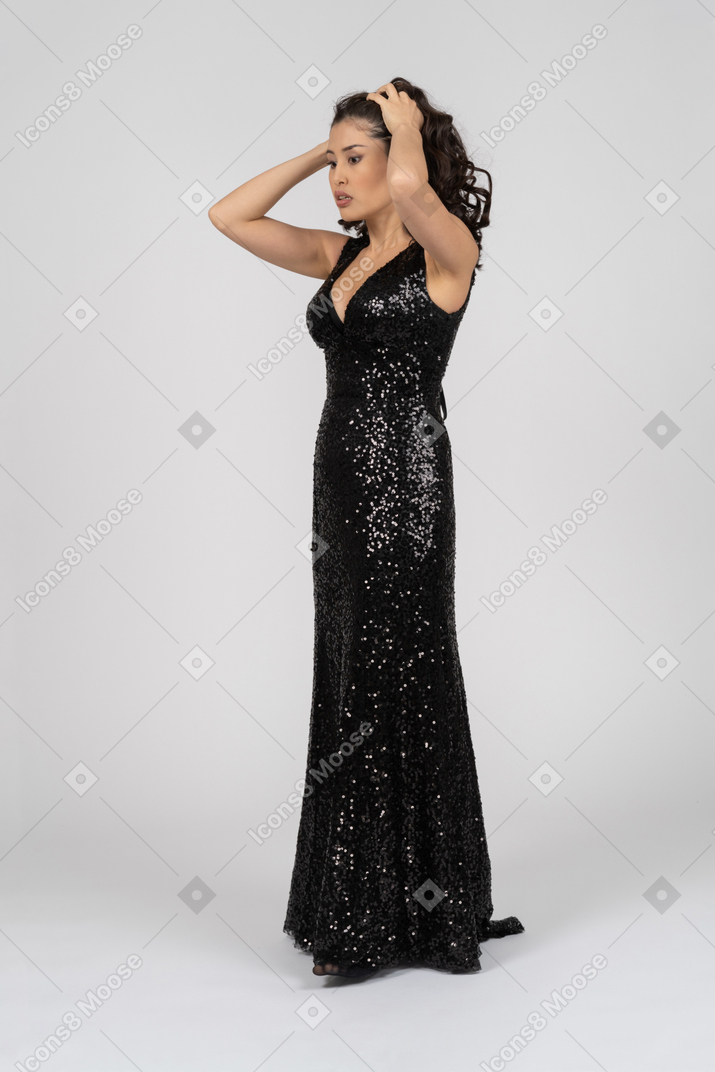 Женщина в черном вечернем платье поднимает руки к голове