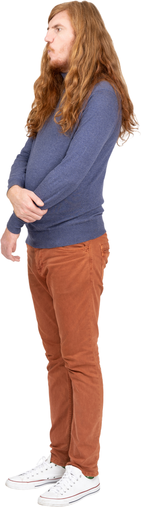 Vista lateral de un joven con ropa informal de pie con los brazos cruzados