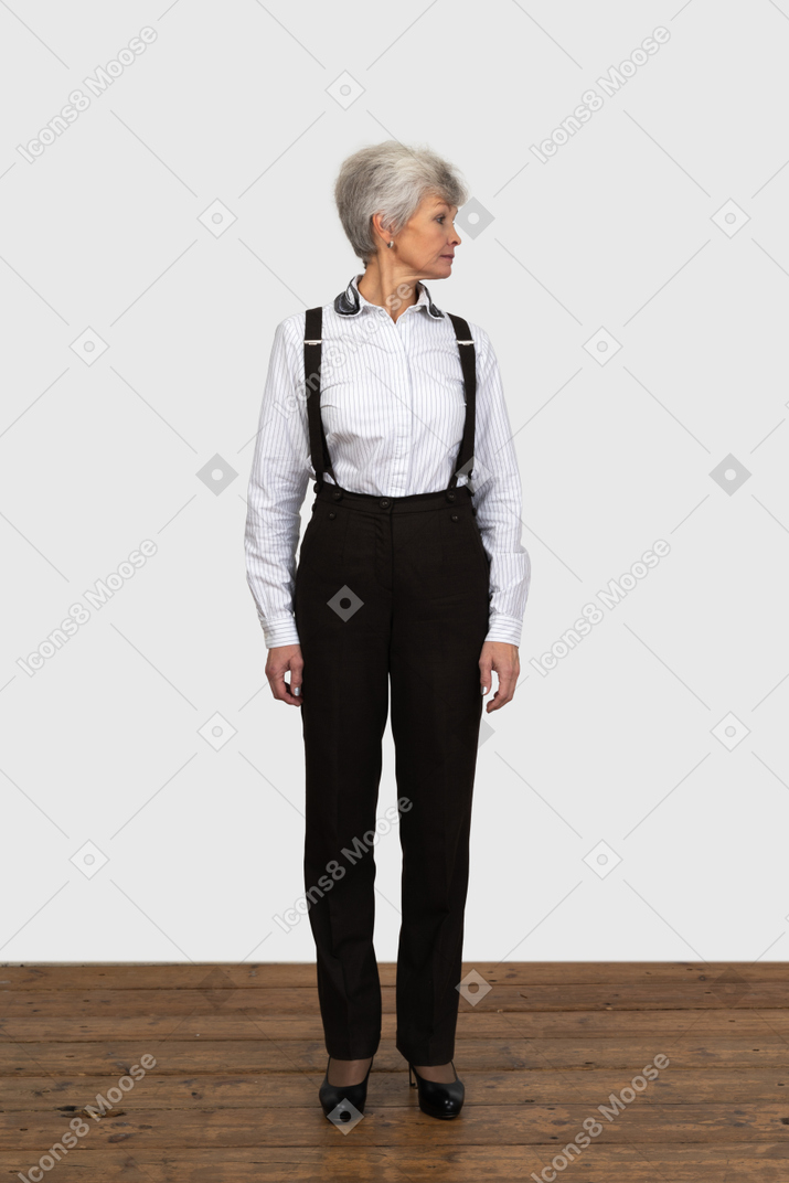 Front view of an old female in office clothes standing still indoors looking aside